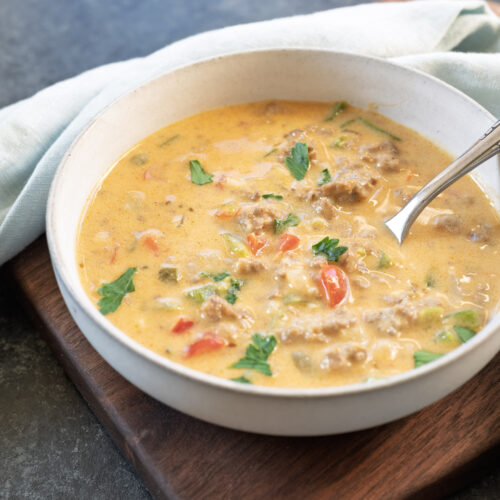 Creamy beer cheese stuffed pepper soup made with ground beef and peppers in a white bowl served on a wood tray.