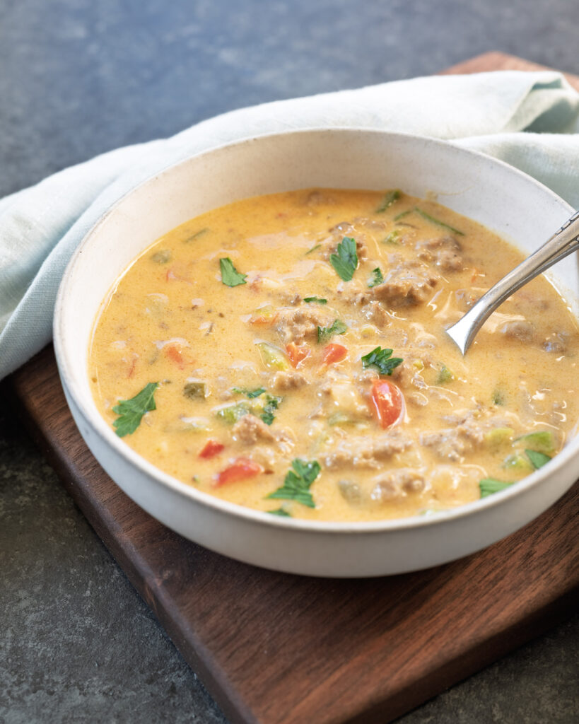 Creamy beer cheese stuffed pepper soup made with ground beef and peppers in a white bowl served on a wood tray.