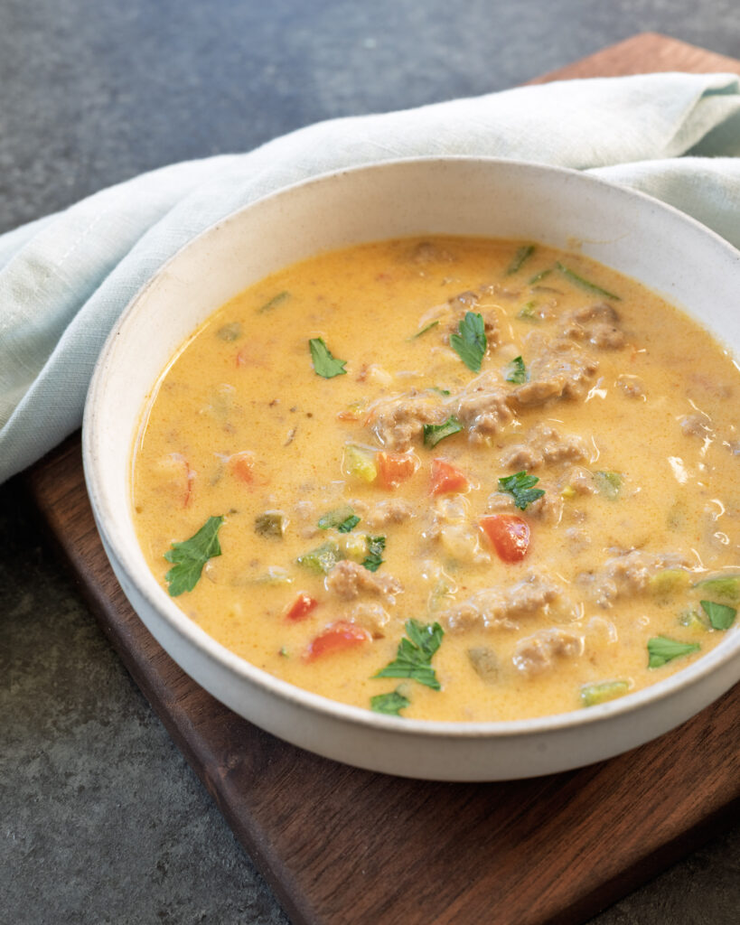 Creamy beer cheese stuffed pepper soup made with ground beef and peppers in a white bowl served on a wood tray.