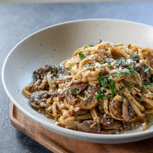 Creamy mushroom pasta in a white pasta bowl as seen from looking towards the food at 45 degrees.