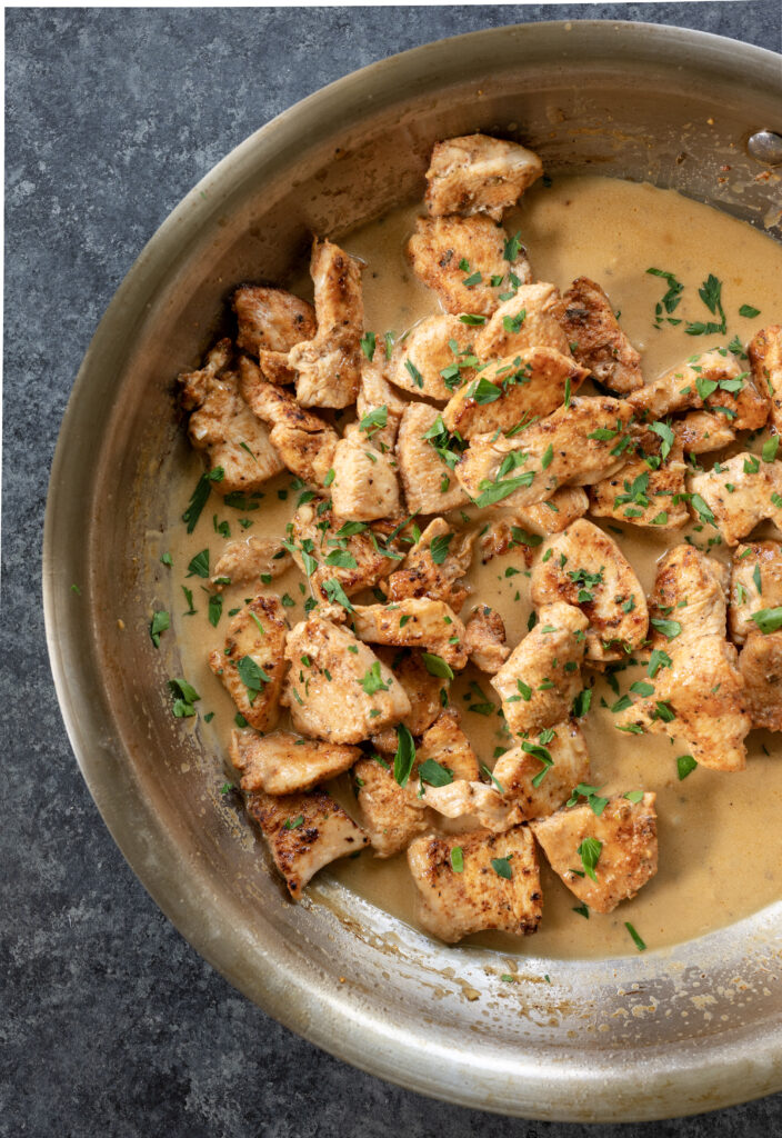 Golden-brown chicken breast pieces in creamy beer pan sauce in a stainless steel skillet.