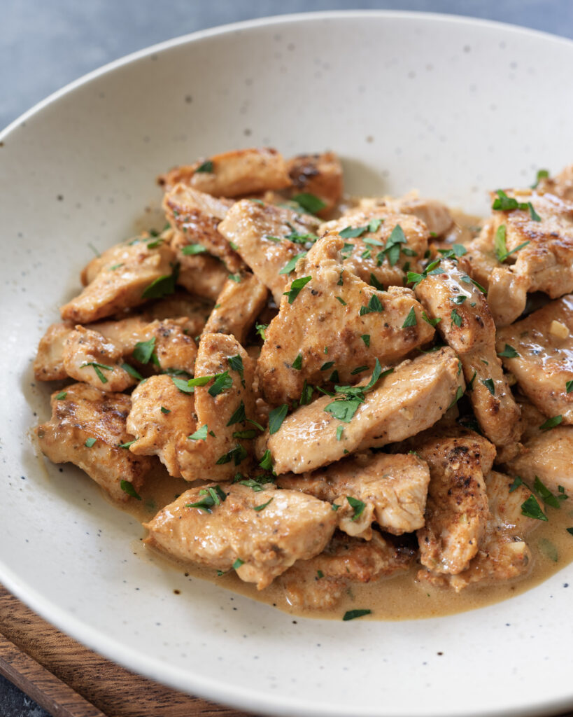 Creamy skillet chicken (date night dinner) with golden-brown chicken breast pieces in a beer pan sauce, garnished with fresh parsley.
