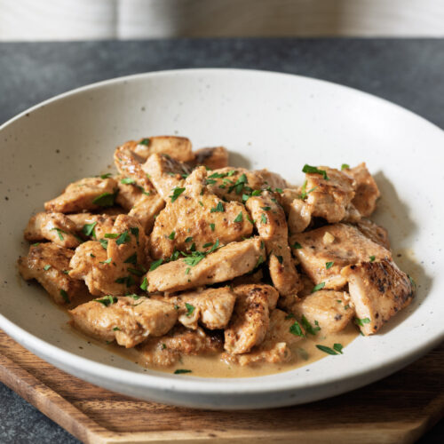 Creamy skillet chicken with golden-brown chicken breast pieces in a beer pan sauce, garnished with fresh parsley.