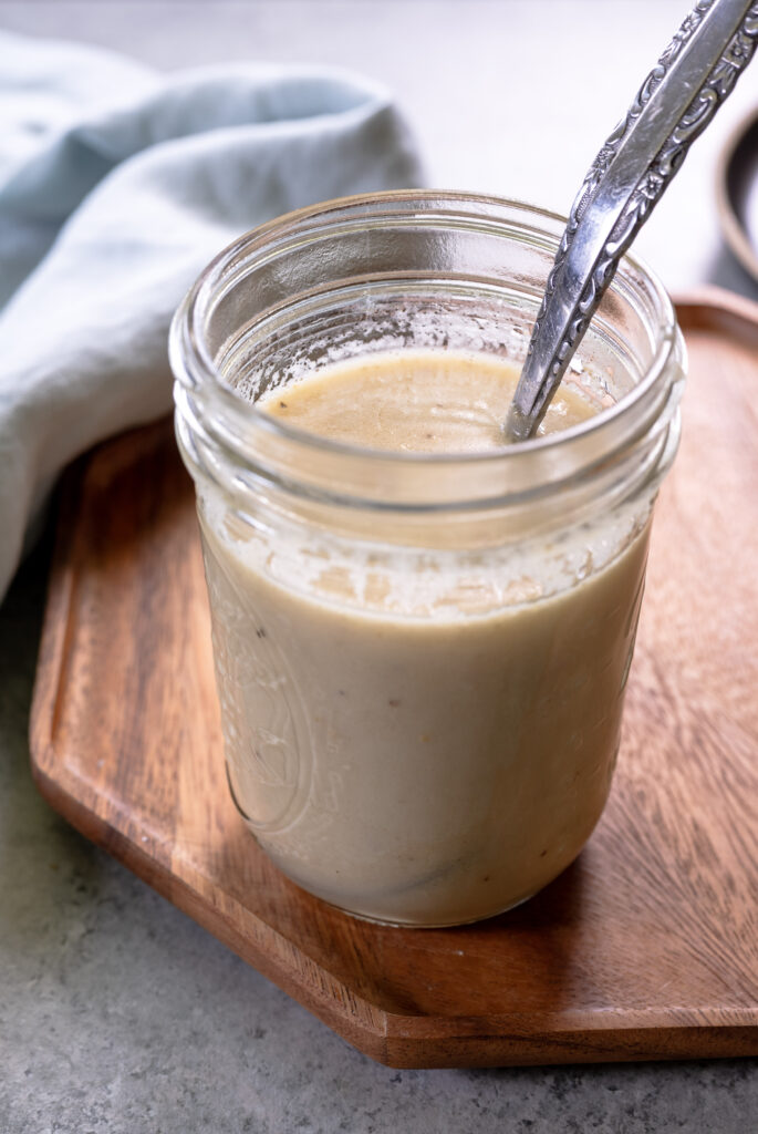Homemade Swedish-style meatloaf gravy in a glass jar with a silver spoon, resting on a wooden tray.