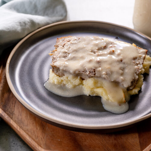 Swedish-style meatloaf topped with creamy homemade gravy, served over mashed potatoes on a dark ceramic plate.