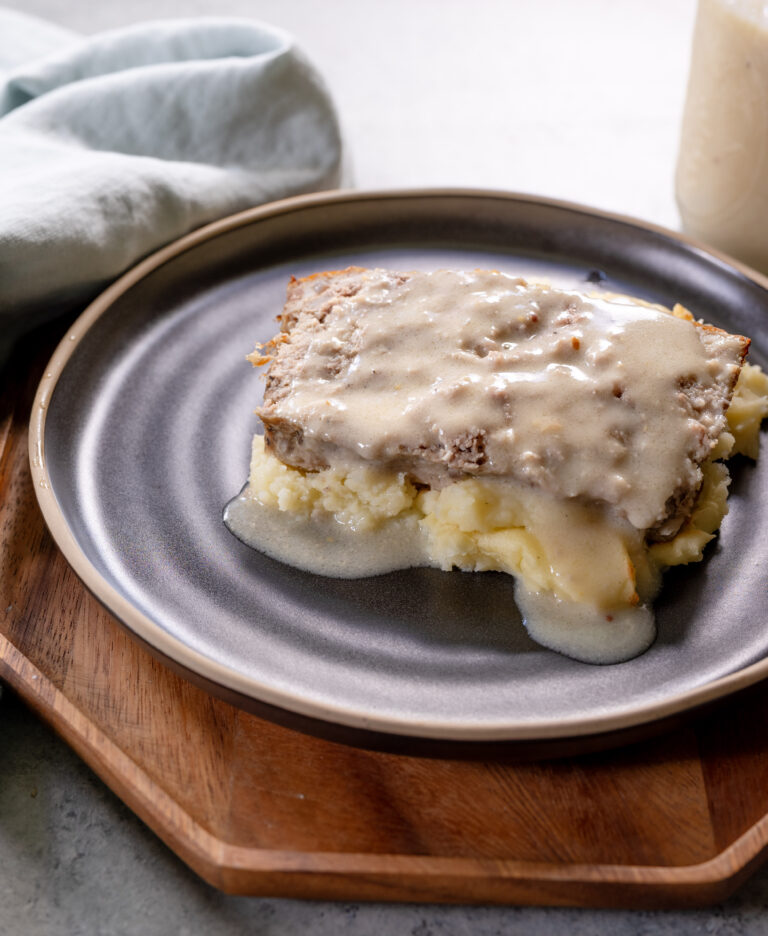 Swedish-style meatloaf topped with creamy homemade gravy, served over mashed potatoes on a dark ceramic plate.